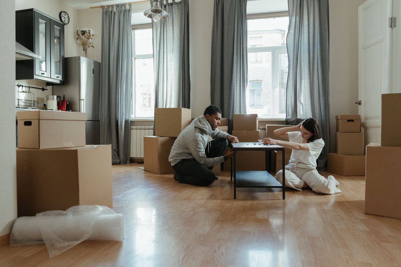 gallery-2 Jeune couple en train de monter des meubles dans leur nouvel appartement, entouré de cartons.